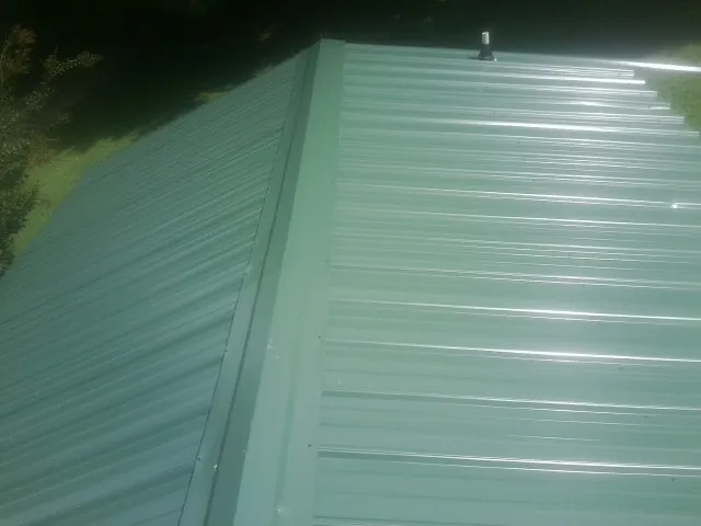 New green metal panels meeting at the ridge of a roof — Flat Roof Repair work by our crew in Cary
