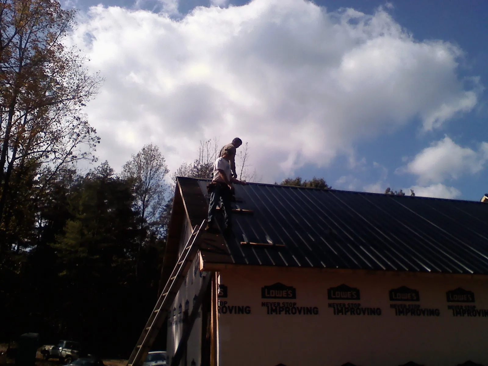 Roofer fastening dark metal panels high against a cloudy sky, from a Roof Inspection job in Cary