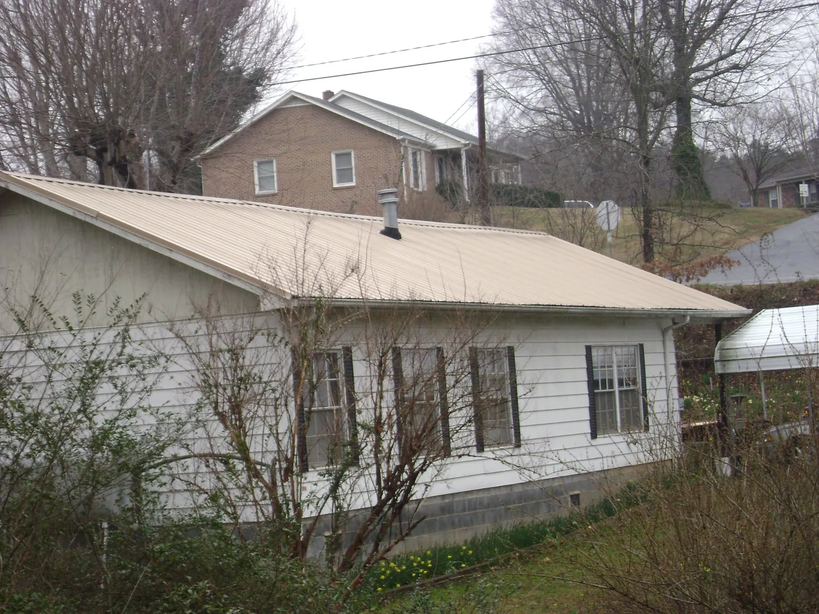Tan metal roof on a white sided house set into a hillside — Commercial Roofing by Roofing Brothers in Cary